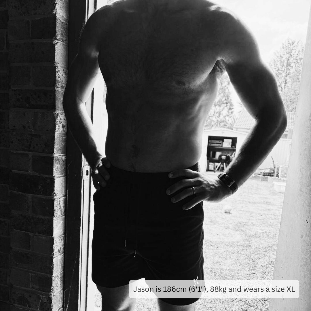 A black and white photo of a shirtless man standing in a doorway wearing dark shorts, with text at the bottom stating 'Jason is 186cm (6'1"), 88kg and wears a size XL'.